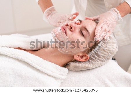 The doctor removes the gel from the patients face and apply a therapeutic cream. Anti acne phototherapy. Beautiful woman during photo rejuvenation procedure. Face skin treatment at cosmetic clinic.