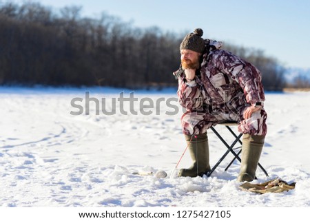 Bearded european sad man is boring while he getting fail at the winter fishing from ice hole on the river