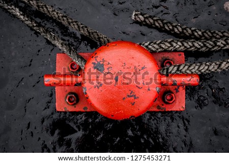 Abstract close up of a rope tied around a red metal cleat on a pier. Used to securely moor a boat when in dock.