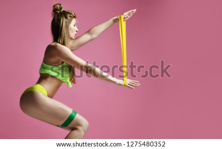 Woman exercising doing postnatal workout. Female fitness instructor working out with a rubber resistance band on modern pink background