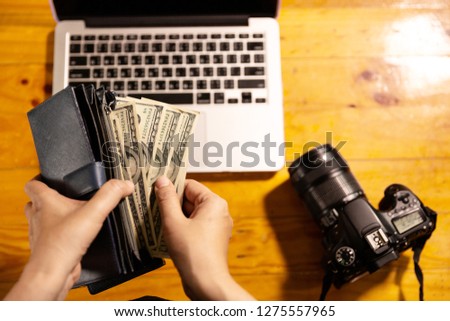 Girl with blue wallet full of money with camera and labtop on wood table.