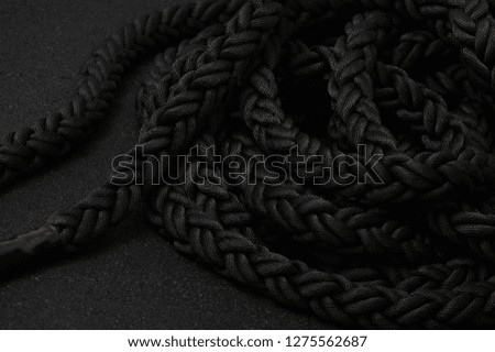 Close up of black thick rope handles lying on the black floor. Black jump rope or skipping rope isolated on white background. Sports, fitness, cardio, martial art and boxing accessories.