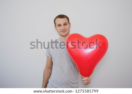 young man in a gray t-shirt holding a heart-shaped balloon and smiling on a white background, Valentine's Day