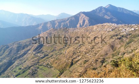Panoramic view of a village on the green and dry slopes of hills