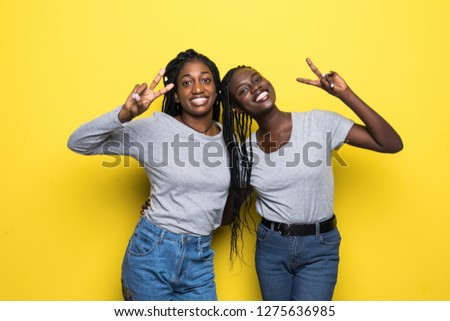 Two happy pretty pretty african women posing together and showing peace gestures while over yellow background