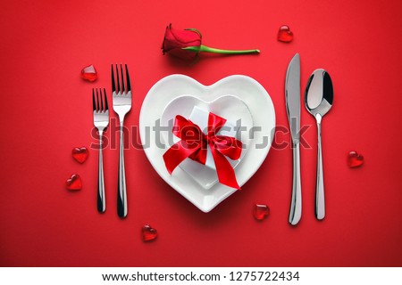Plates in shape of heart, holidays table setting with a gift box on red background
