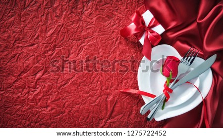 Plates in shape of heart, holidays table setting with a gift box on red background. Valentines day concept