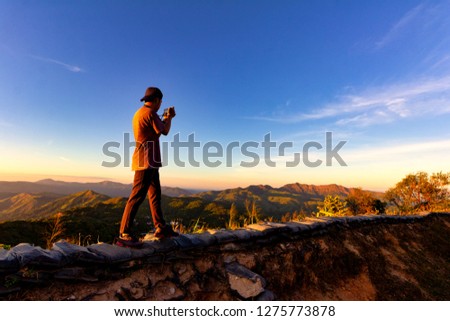 Silhouette of traveler taking photo at top of mountain.