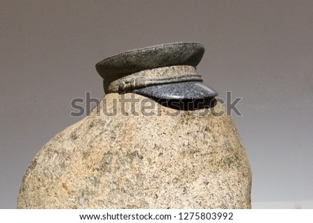 A military cap lying on a stone. The shadow of the visor of the headdress falls on the stone
