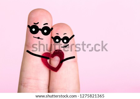 fingers with painted faces in glasses on a pink background, concept of an engaged couple, blank for Valentine's Day