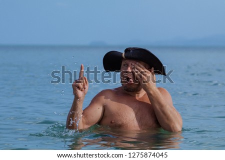 Emotional man in a black French hat pirate posing in the surf in the water on the beach.