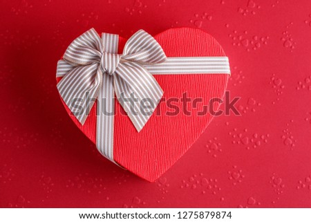 Gift box in the shape of a heart with a ribbon on a red background. The concept is suitable for love stories, birthdays and Valentine's Day
