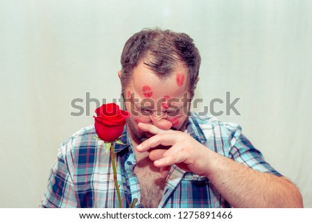 Bearded mature man with a red rose.There are traces of lipstick on his face. He's allergic to flowers.