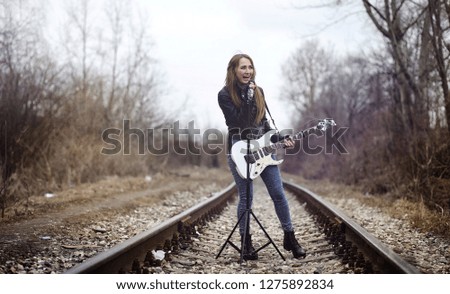 Beautiful young girl rocker with electric guitar. A rock musician girl in a leather jacket with a guitar sings. A rock band soloist plays the guitar and screams into microphone.
