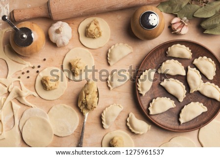 Cooking traditional Russian food. Forming small handmade dumplings, stuffing round flat pieces of dough with potato and mushrooms on kitchen table, closeup