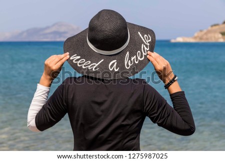 
woman with black hat by the sea , written on hat  need a break 