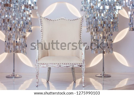 Interior design. Living room space: white stylish chair and glamorous lamps at the background of white wall