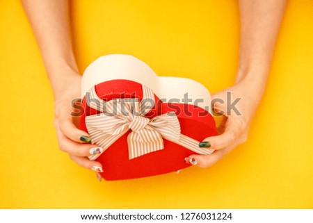 Gift box in the shape of a heart with a ribbon on in female hands. The concept is suitable for love stories, birthdays and Valentine's Day