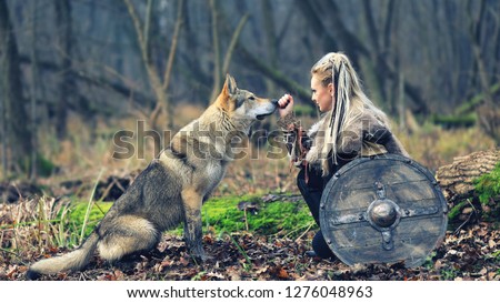 Viking woman warrior with braided hair holding shield close to wild wolf in forest - Outdoor warrior princess alone in woods with wolf – movie theme - cinematic tone filter Royalty-Free Stock Photo #1276048963