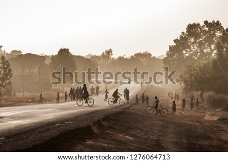 Highway at the exit of Ouagadougou, Burkina Faso, at dusk with silhouetted people. African scenery. Royalty-Free Stock Photo #1276064713