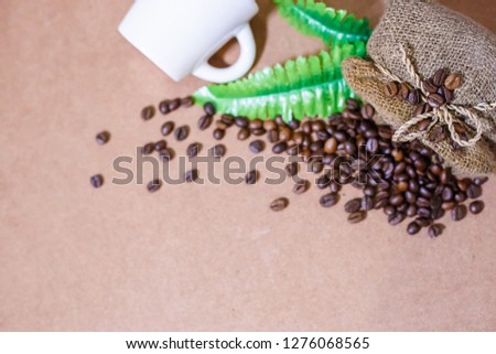 Close up coffee beans and Blur a white cup of coffee with coffee beans in coffee burlap bag on old wooden background. Copy space for text.