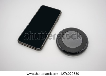 Black mobile phone placed by black round shape wireless charger isolated on white background.