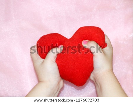 soft red heart in hands of  child on  pink background