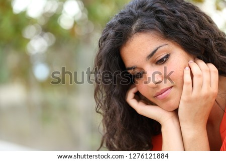 Pensive melancholic woman looking down sitting alone in a park