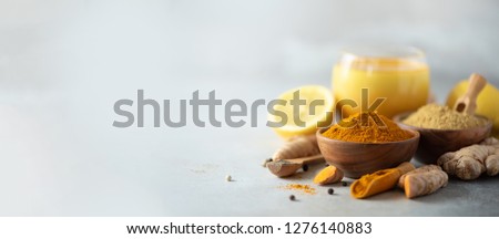 Healthy vegan turmeric latte or golden milk, turmeric root, ginger powder, black pepper over grey background. Spices for ayurvedic treatment. Alternative medicine concept. Banner with copy space. Royalty-Free Stock Photo #1276140883