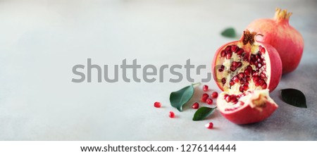 Ripe pomegranate fruit with green leaves on grey concrete background. Banner with copy space. Vegan, healthy diet concept.