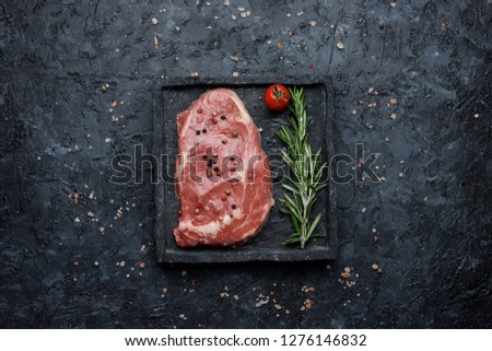 Food background. Raw rib eye steak with tomatoes and rosemary on black background top view