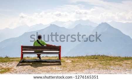 A man sits on a wooden bench at the top of the Alps and looks at the beautiful mountain landscape.