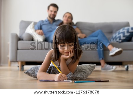 Cute kid girl playing on warm floor at home, preschool little girl drawing with colored pencils on paper spending time with family in living room, creative child activity, underfloor heating concept Royalty-Free Stock Photo #1276178878