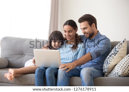 Happy family with kid daughter enjoy using laptop apps, making online call together, smiling parents and child girl relaxing having fun watching video on computer, doing internet shopping at home