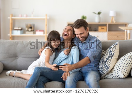 Cheerful family vloggers with child daughter taking selfie, recording vlog, making video call on phone having fun together in living room, parents and kid girl laugh using cellphone funny online app Royalty-Free Stock Photo #1276178926