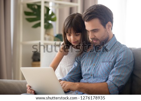 Father and kid girl using laptop at home looking at screen choosing goods online, happy dad talking to child daughter showing new computer application watching video, doing internet shopping together Royalty-Free Stock Photo #1276178935