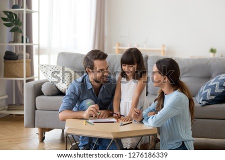 Happy family with kid playing together, caring mom and dad smiling teaching little daughter to draw with color pencils, mother and father having fun with cute child help in creative weekend activity Royalty-Free Stock Photo #1276186339
