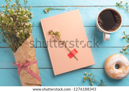 Notebook and a delicious snack, hot coffee and donut. Above view with spring flowers on a blue colored table