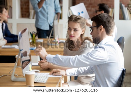 Executive manager mentor teaching intern employee giving instructions showing new online project pointing on computer screen, serious worker helping explain colleague listen work task look at monitor Royalty-Free Stock Photo #1276205116