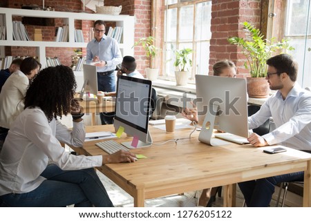 Multi-ethnic employees working on computers in modern office room, corporate staff team people diverse workers group using desktop monitors sitting at desks in open shared coworking space together Royalty-Free Stock Photo #1276205122