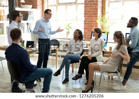 Diverse business team employees listening to male manager coach speaking at group office meeting, mentor executive leader talking during briefing, multi-ethnic workers engaged in corporate training Royalty-Free Stock Photo #1276205206