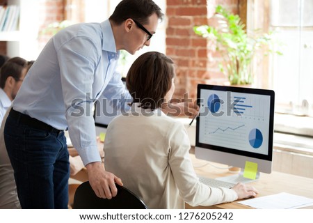 Executive manager mentor helping employee intern preparing online statistical report in office, ceo teaching training explaining worker computer data graphs charts stats analysis pointing on monitor Royalty-Free Stock Photo #1276205242