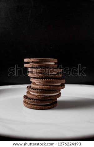 A pile of cream biscuits on a white plate against a dark background