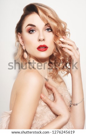 Beautiful woman in earrings and ring. Model in jewelry, diamonds. Fashion portrait of young girl with jewelry. Blond girl with cerly air and red lips. Perfect make-up. The girl in the pink coat