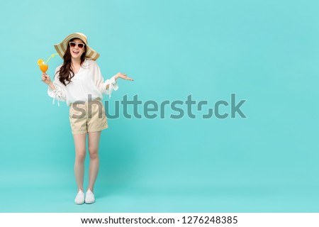 Happy Asian woman in summer casual clothes holding a glass of fruit juice drink studio shot isolated on light blue backgroud with copy space