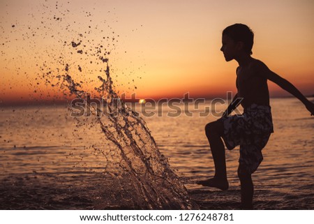 One happy little boy playing on the beach at the sunset time.  Kid having fun outdoors. Concept of summer vacation.