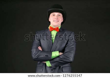 Cheerful happy man in a bowler hat is standing with crossed arms and smiling on a black background.