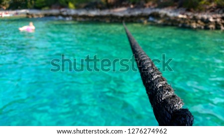 Selective focus on the anchor rope of the arrived boat. The tourist in water near stone coast of Brock island at sea in Croatia. Boat tour entertainment. Nautical and marine vacation background.