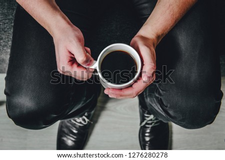 Top view for coffee held by a sitting man. The man is holding a white mug with black coffee in his hands. The concept of rest, expectations, and strengthening of coffee.