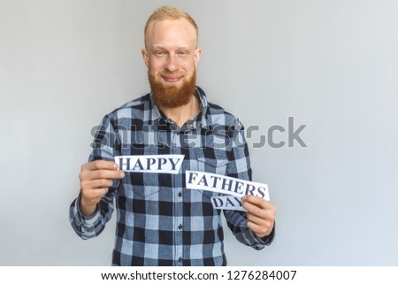 Red hair mature man standing isolated on grey wall holding happy fathers day congratualition letters looking camera smiling joyful
